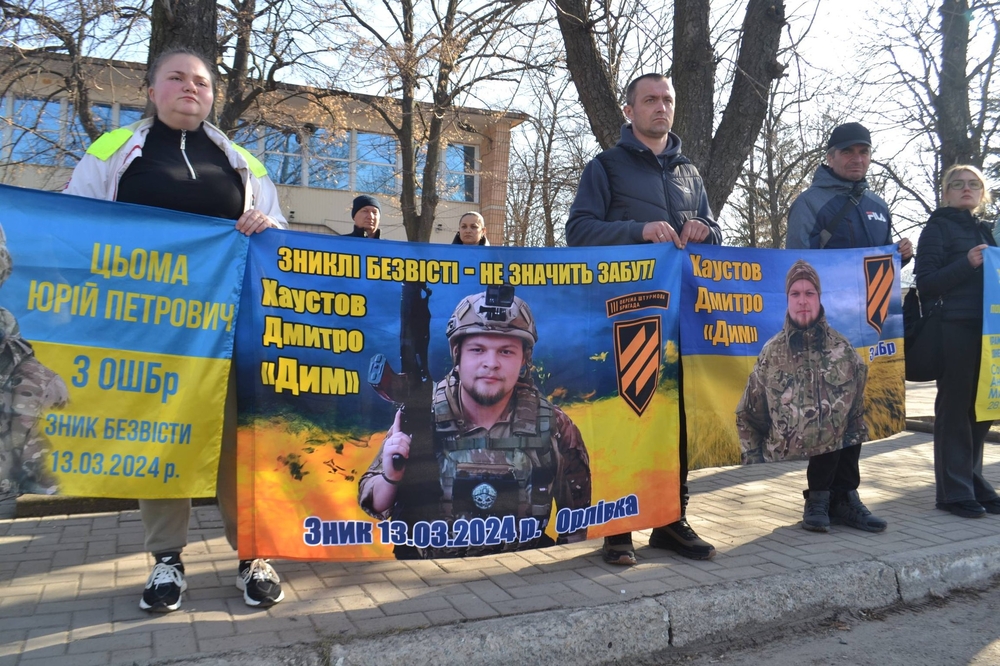 Люди стоять з прапорами, на яких зображені воїни