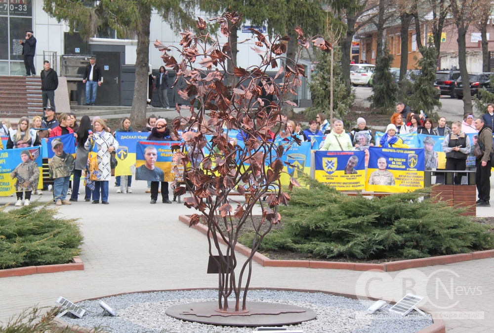 Позаду інсталяції зібралися люди з плакатами