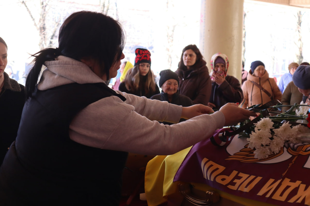 Жінка кладе квіти на труну полеглого військового Дмитра Богзи