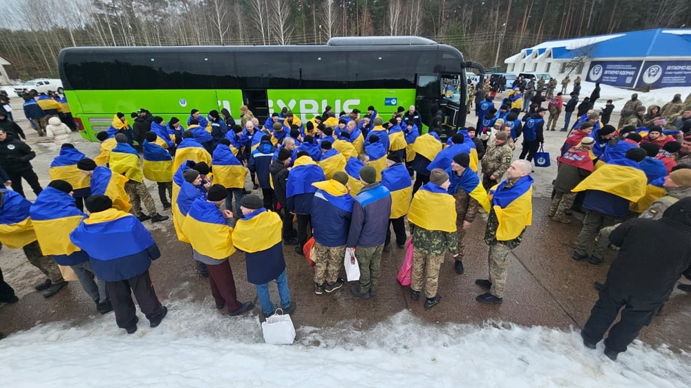 Звільнені з російського полону військові стоять з прапорами біля автобусів