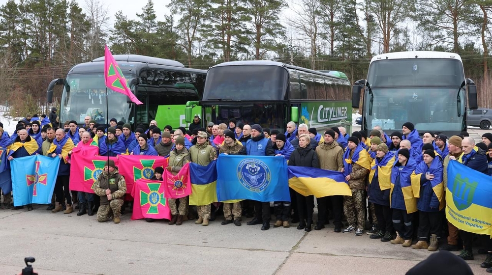 Звільнені з російського полону військові стоять з прапорами біля автобусів