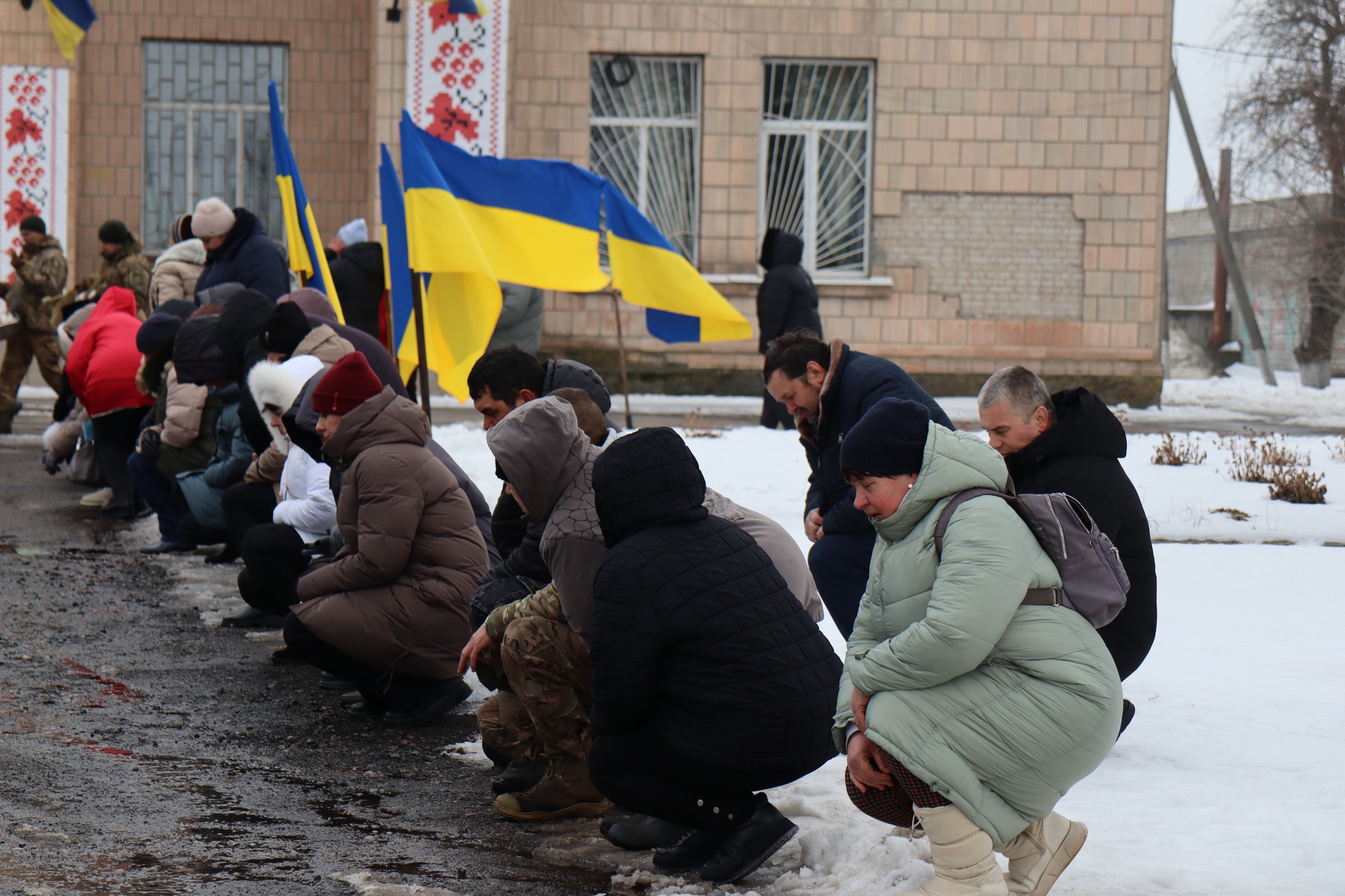 Люди стоять на колінах на прощанні з Миколою Сичовим з Онуфріївської громади