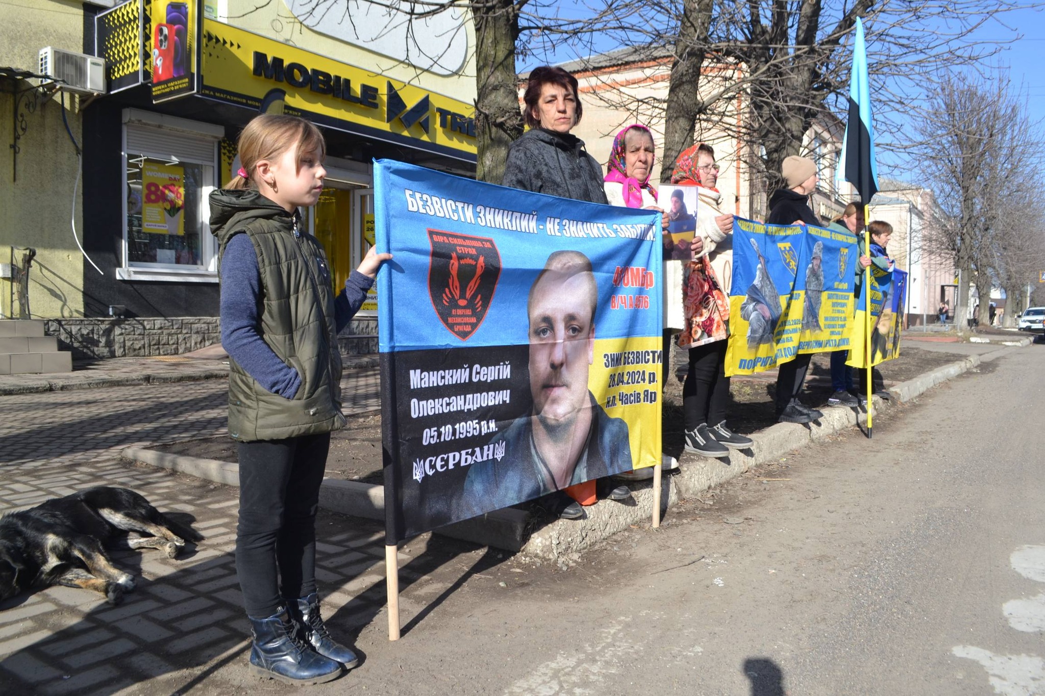 Жителі Новоукраїнки стоять з прапорами, на яких зображені воїни