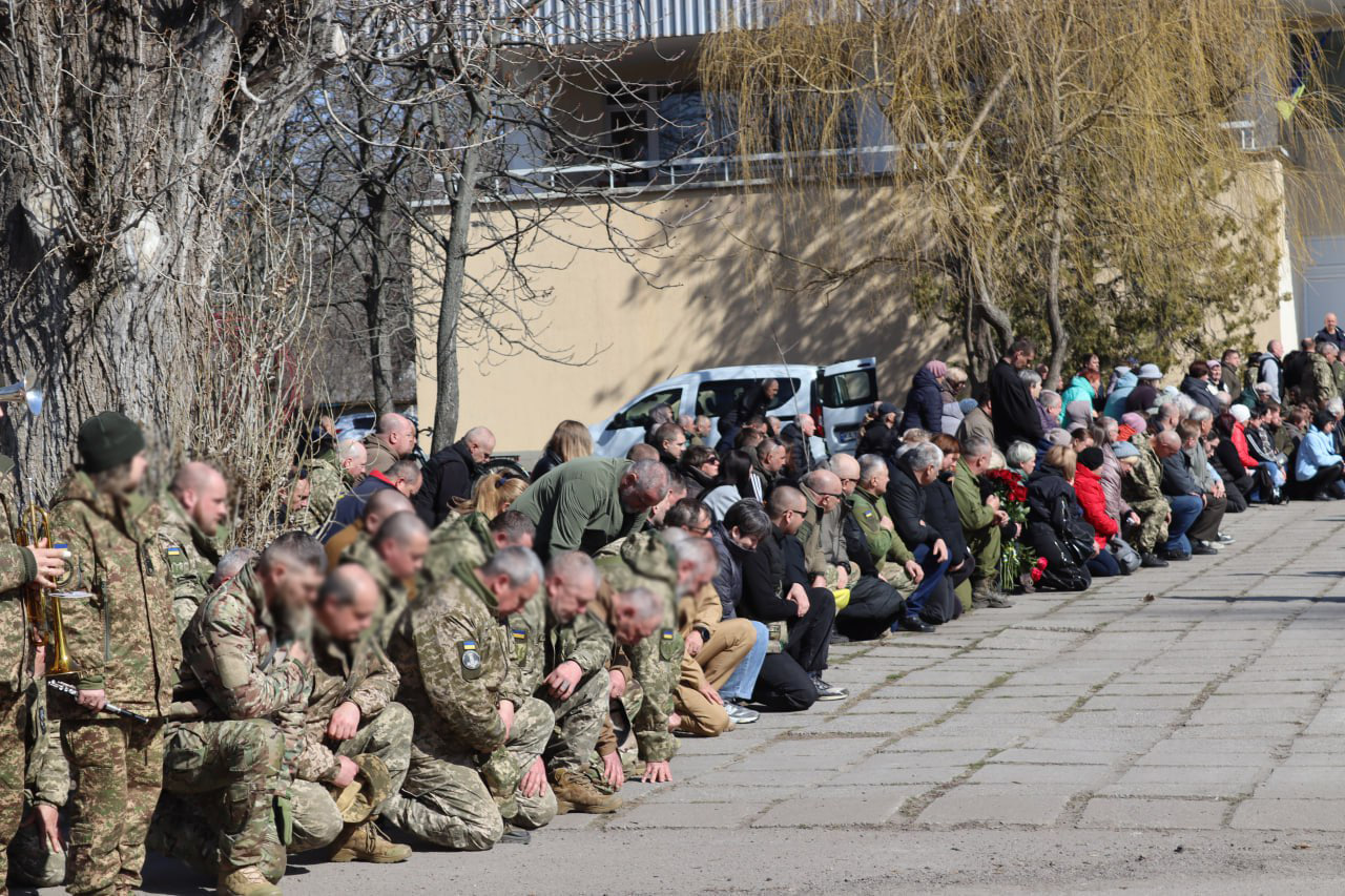Багато людей схилились на колінах та зустрічають колону прощання із загиблим Дмитром Михайликом