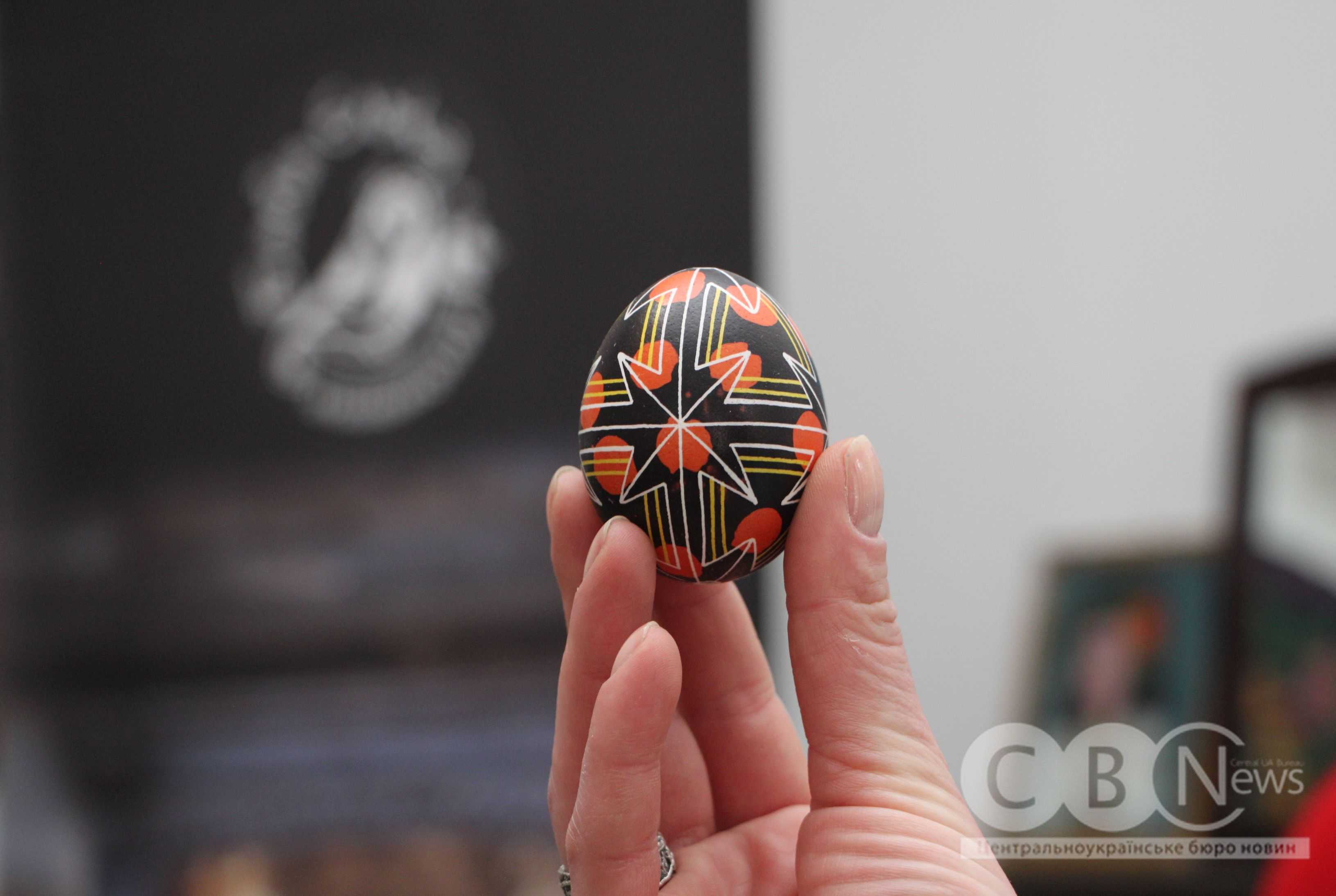 У руках тримають чорну писанку