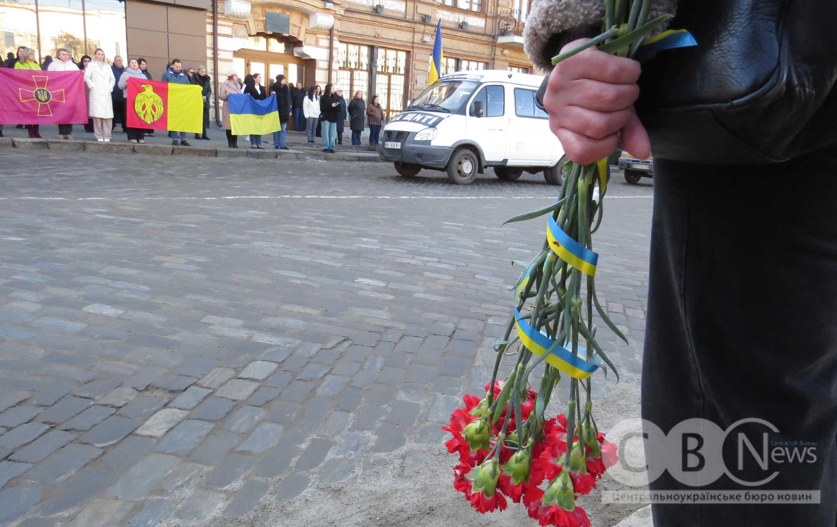 Людина тримає квіти, поки середмістям Кропивницького проїжджає траурний кортеж