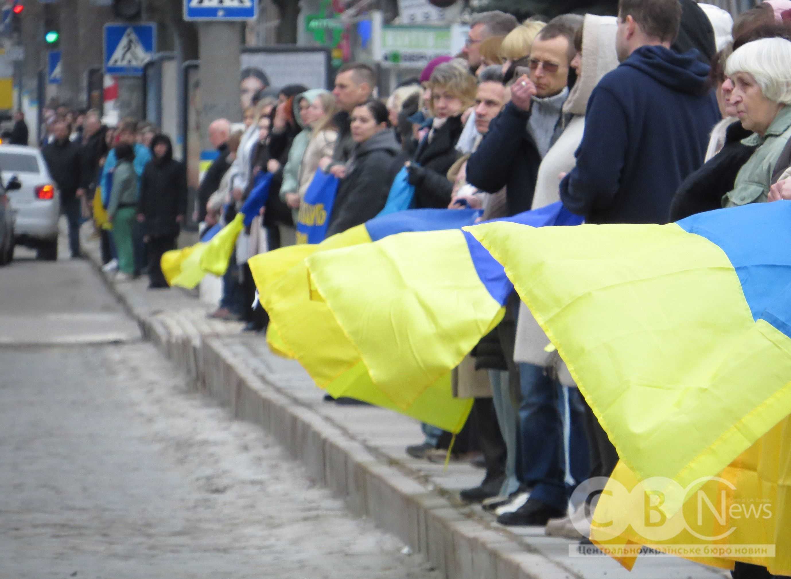 Люди стоять в ряд з державними прапорами України