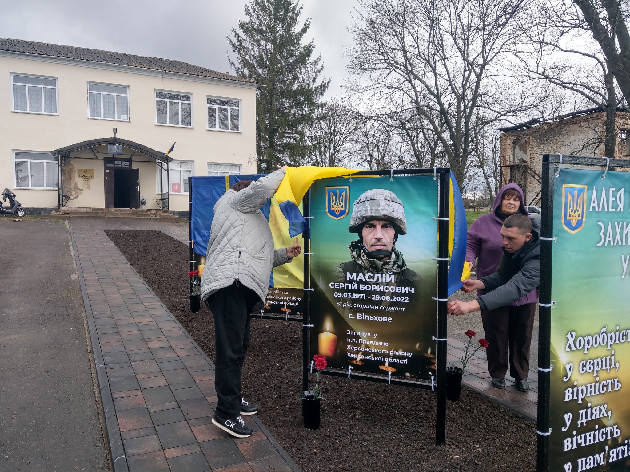 Жінка відкриває портрет загиблого воїна на Алеї слави у Благовіщенській громаді