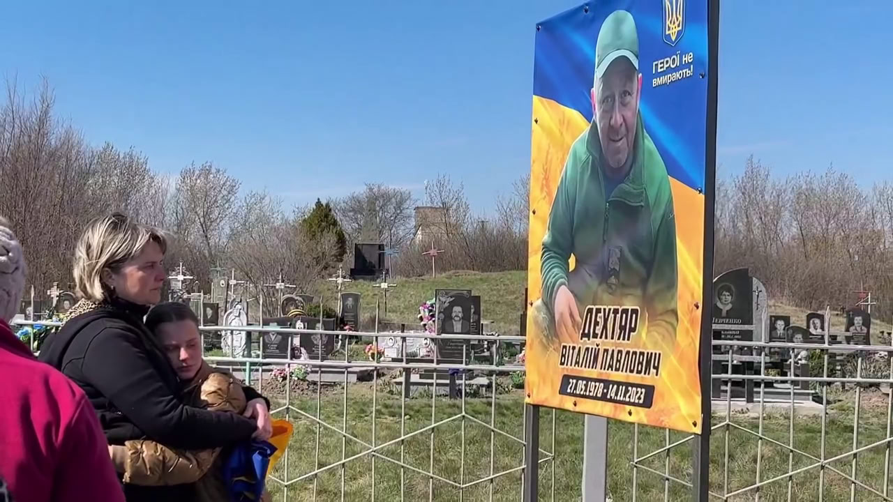 Жінка та дівчина обіймаються перед портретом загиблого воїна з Новомиргородської громади