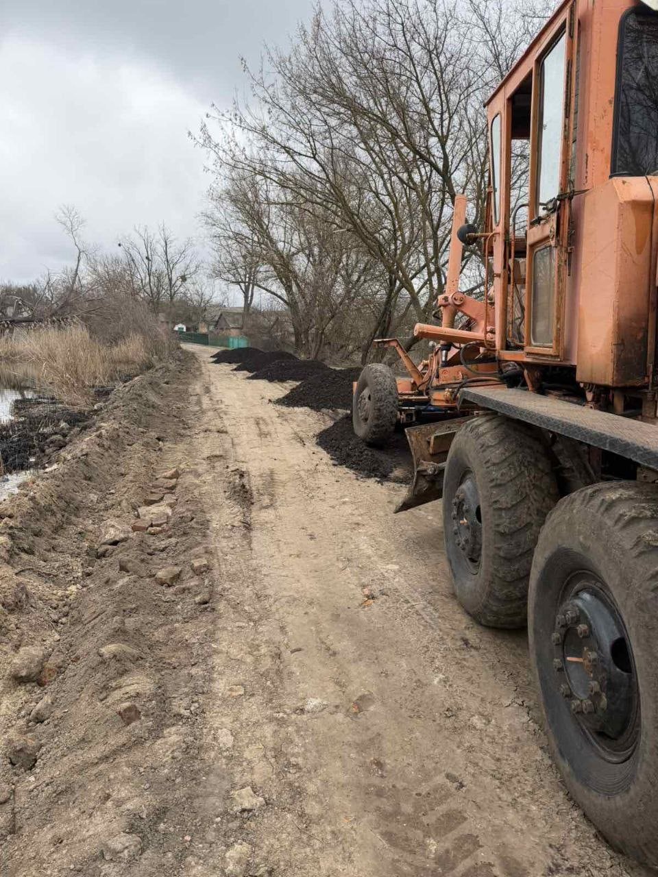 Грейдер ремонтує дорогу через греблю у Олександрівській громаді